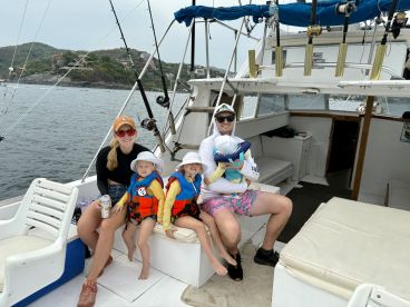 A family enjoying a day on a fishing boat, with two children in life jackets and adults relaxing in the cabin area.