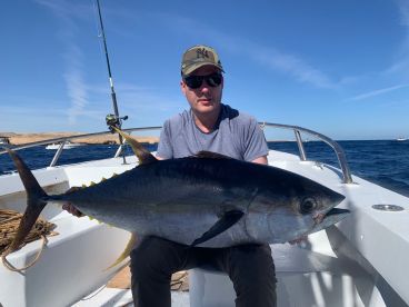 Angler displaying a large Bluefin Tuna aboard a fishing boat, showcasing a successful catch in a sunny marine environment.
