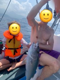 A young angler in a life jacket proudly displays a caught fish while fishing on a boat, enjoying a sunny day on the water.