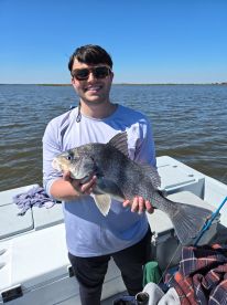 An angler proudly displaying a large Black Drum caught during a fishing trip on calm waters.