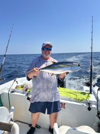 An angler proudly displaying a large Yellowtail on a fishing boat, enjoying a sunny day on the open water.