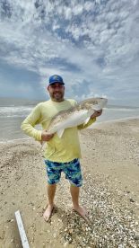 An angler proudly displaying a large Redfish on the beach, showcasing a successful day of fishing.