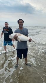 Two anglers enjoying a successful day at the beach, with one proudly displaying a large Redfish caught in the surf.