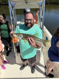 An angler proudly displaying a Snook while fishing on a boat, surrounded by fellow anglers in a scenic waterway.