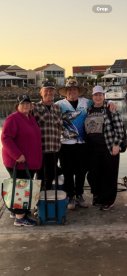 A group of four anglers posing together on the dock at sunrise, showcasing their fishing spirit with a cooler in the background.