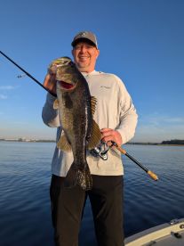 An angler proudly displaying a large Largemouth Bass while fishing on a calm lake, showcasing a beautiful morning backdrop.