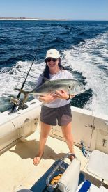 A young woman proudly displaying a large Jack Crevalle while fishing on a boat in open waters.
