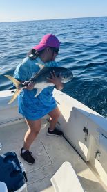 A young angler reeling in a large fish while fishing on a boat in open waters.