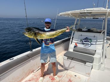 Angler proudly displaying a large Mahi Mahi aboard a sport fishing boat in clear blue waters.
