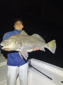 Angler proudly displaying a large Snapper caught during a night fishing trip, showcasing the excitement of a successful catch.