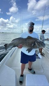 Angler proudly displaying a large Black Drum aboard a fishing boat, enjoying a day on the water.