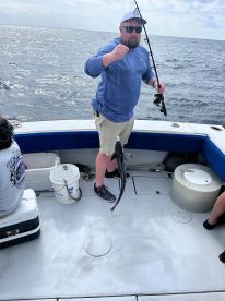 An angler reeling in a fish while fishing on a charter boat in open waters.