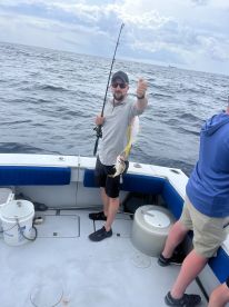 Angler reeling in a Yellowtail Snapper while fishing on a charter boat in open waters.