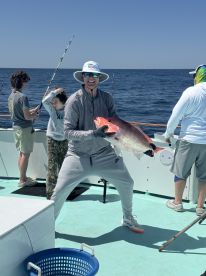 A young angler proudly displays a large Red Snapper while fishing on a charter boat, surrounded by family members enjoying a day on the water.