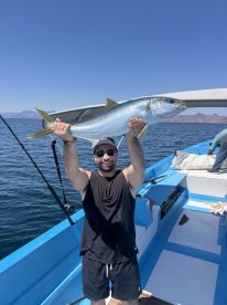 An angler proudly displaying a large Yellowtail while fishing on a boat in open waters.