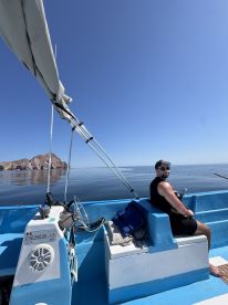 A relaxed angler seated inside a blue fishing boat, enjoying a calm day on the water with scenic coastal views.