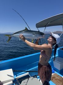 Angler proudly displaying a large Yellowtail while fishing on a boat in clear blue waters.