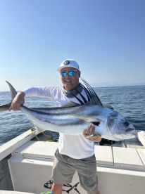 Angler proudly displaying a large Roosterfish while fishing offshore, showcasing the excitement of a successful catch.