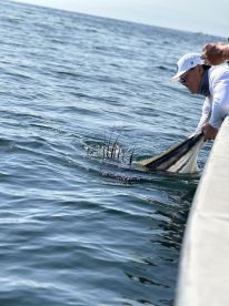 An angler is actively reeling in a large fish, showcasing the thrill of deep-sea fishing in open waters.