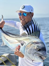 Angler proudly displaying a large Roosterfish while fishing in open waters, showcasing a successful catch.