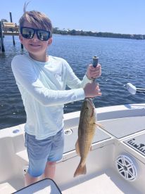 Young angler proudly holding a large fish while fishing from a boat in a calm waterway.