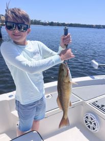 A young angler proudly displaying a large Redfish while fishing on a sunny day.