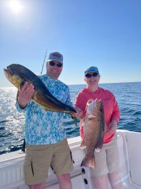 Two anglers proudly displaying their catch, a Mahi Mahi and a Snapper, while fishing on a sunny day in open waters.