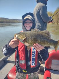 A young angler proudly displaying a large Smallmouth Bass while fishing on a river, showcasing a joyful moment on the water.