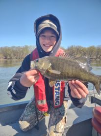 Young angler proudly holding a large Smallmouth Bass while fishing on a river, showcasing a successful day on the water.