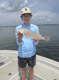 Young angler proudly holding a Redfish while standing on the deck of a boat in a coastal fishing environment.