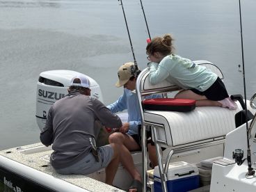 A young girl watches intently as two adults prepare fishing gear on a comfortable boat interior, showcasing a family-friendly fishing experience.